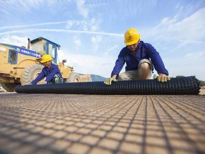 Two road workers are putting the black geogrid on the roadbase.