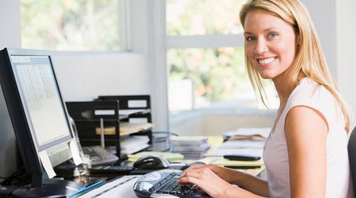 A young lady is smiling at us in front of a computer.